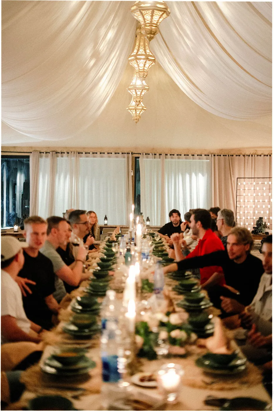 De hele groep aan het diner langs een lange tafel met kaarsen, in een tent.
