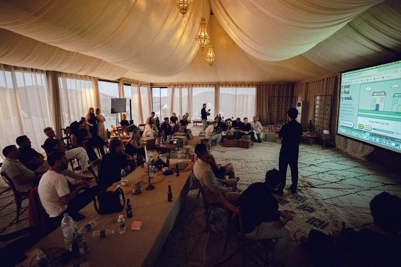 De hele groep in de grote tent kijkt naar een demo op een projectiescherm.
