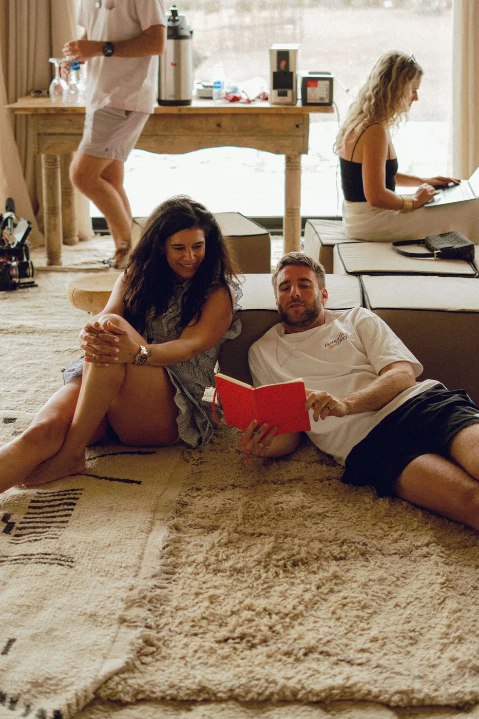 Twee deelnemers zitten op een kleed; een van hen leest voor uit een rood notitieboek.
