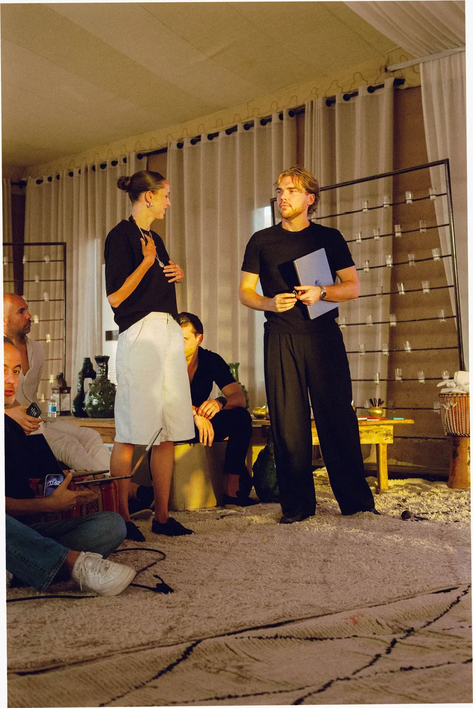 Twee deelnemers presenteren staand in de tent, terwijl anderen zittend luisteren.